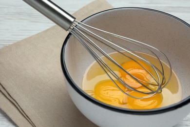 Photo of Whisk and eggs in bowl on white table, closeup