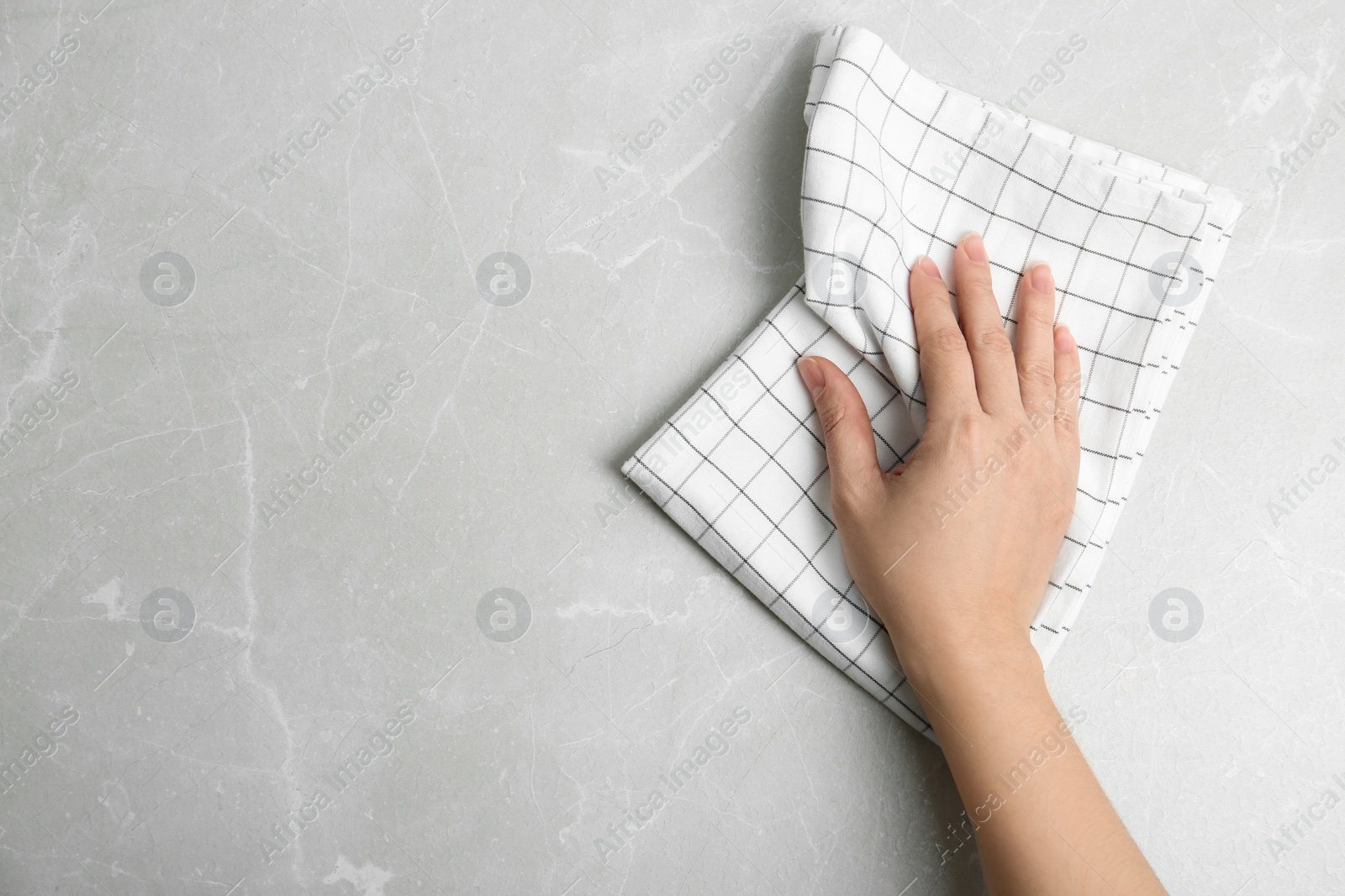 Photo of Woman wiping light grey marble table with kitchen towel, top view. Space for text