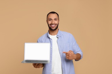 Smiling young man showing laptop on beige background