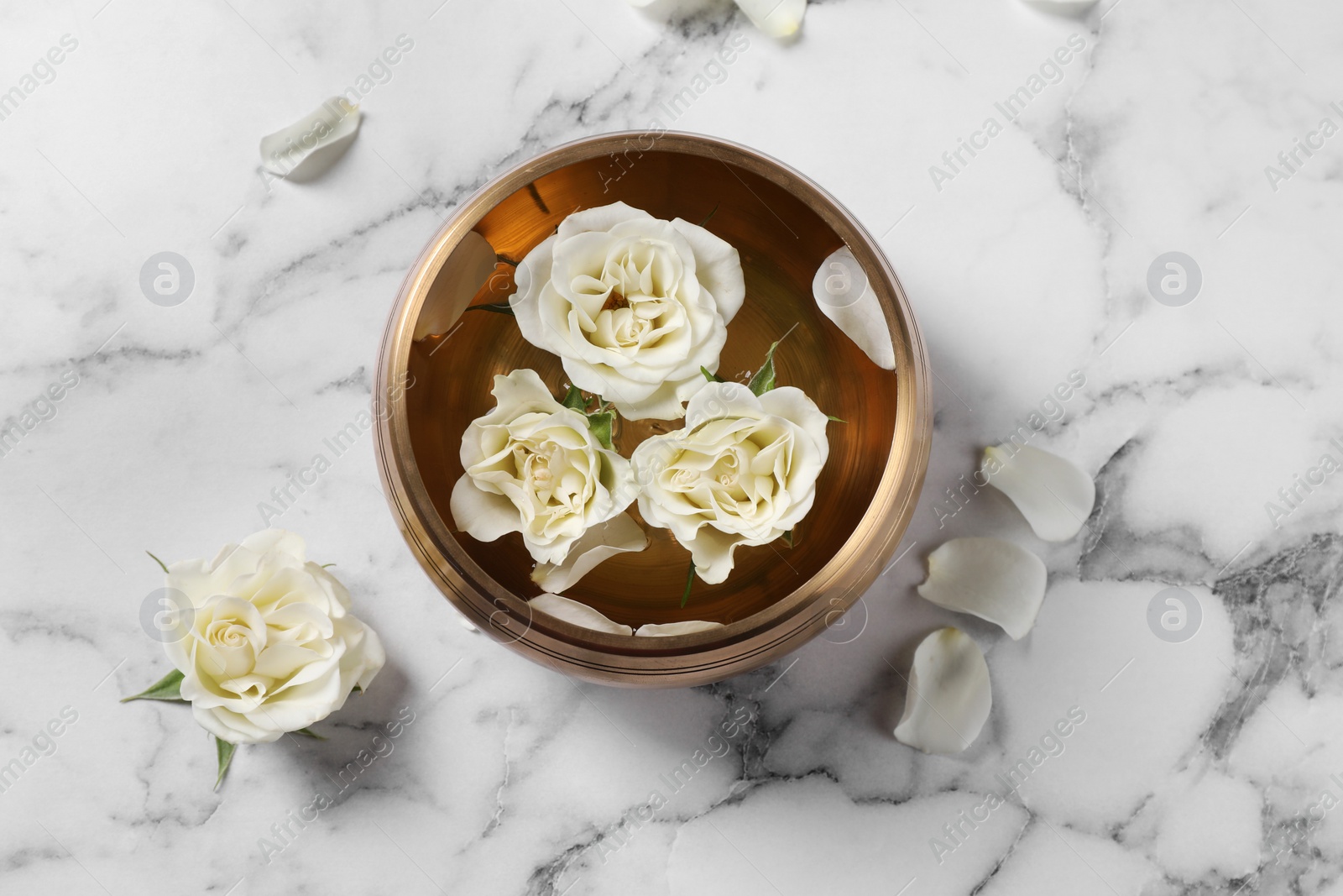 Photo of Tibetan singing bowl with water and beautiful roses on white marble table, top view