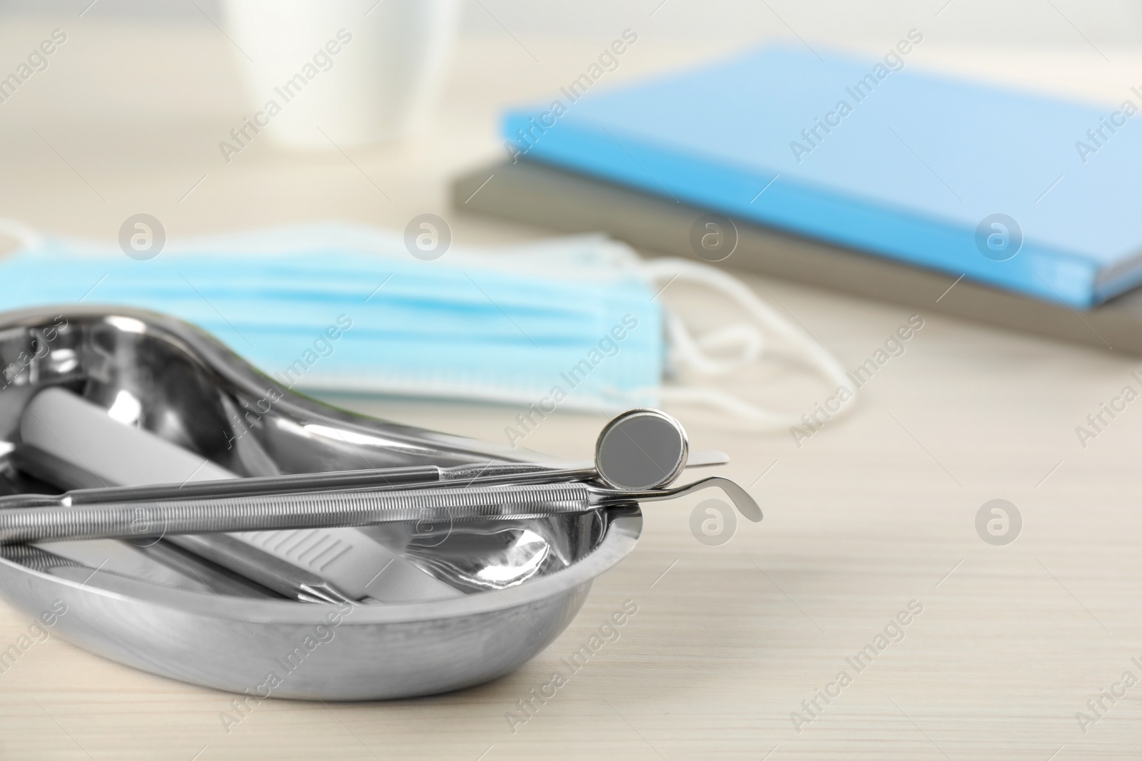 Photo of Kidney shaped tray with set of dentist's tools on wooden table, closeup. Space for text