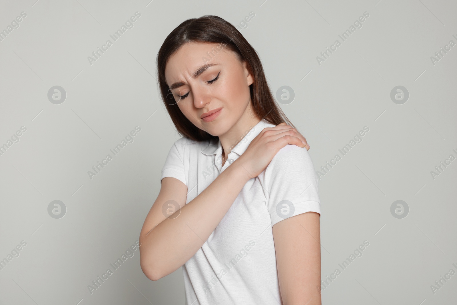 Photo of Young woman suffering from pain in her shoulder on light grey background. Arthritis symptoms