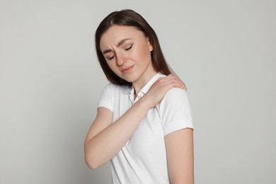 Photo of Young woman suffering from pain in her shoulder on light grey background. Arthritis symptoms