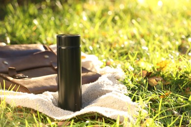 Photo of Black thermos and bag with blanket on green grass outdoors, space for text