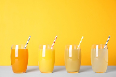 Photo of Different fresh juices in glasses on light table against orange background