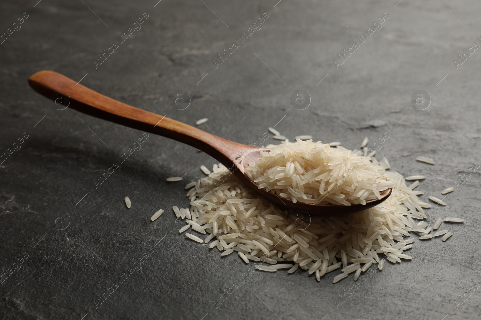 Photo of Raw basmati rice and wooden spoon on black table