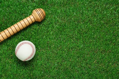 Photo of Wooden baseball bat and ball on green grass, flat lay. Space for text