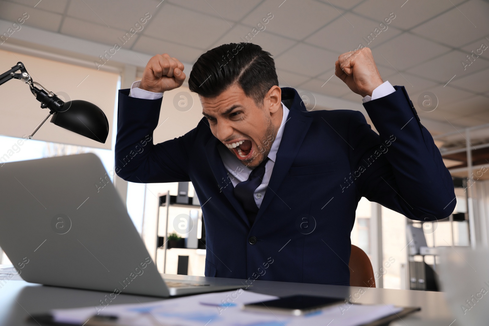 Photo of Emotional businessman with laptop at table in office