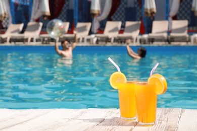 Photo of Refreshing cocktails and young couple in swimming pool on background. Space for text