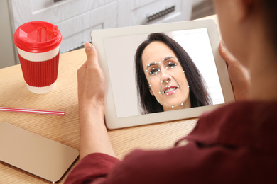 Image of Woman using tablet with facial recognition system in office, closeup. Biometric verification