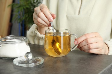 Woman stirring sugar in tea at grey table, closeup