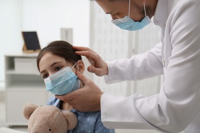 Pediatrician examining little girl in hospital. Doctor and patient wearing protective masks