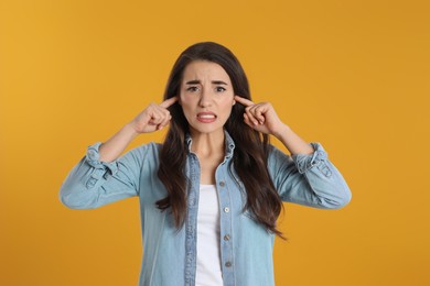 Photo of Emotional young woman covering ears with fingers on yellow background