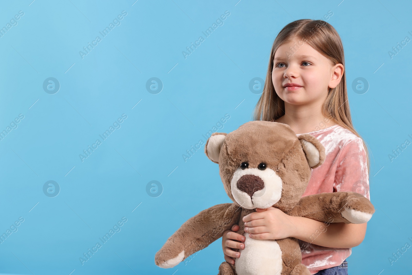 Photo of Cute little girl with teddy bear on light blue background. Space for text