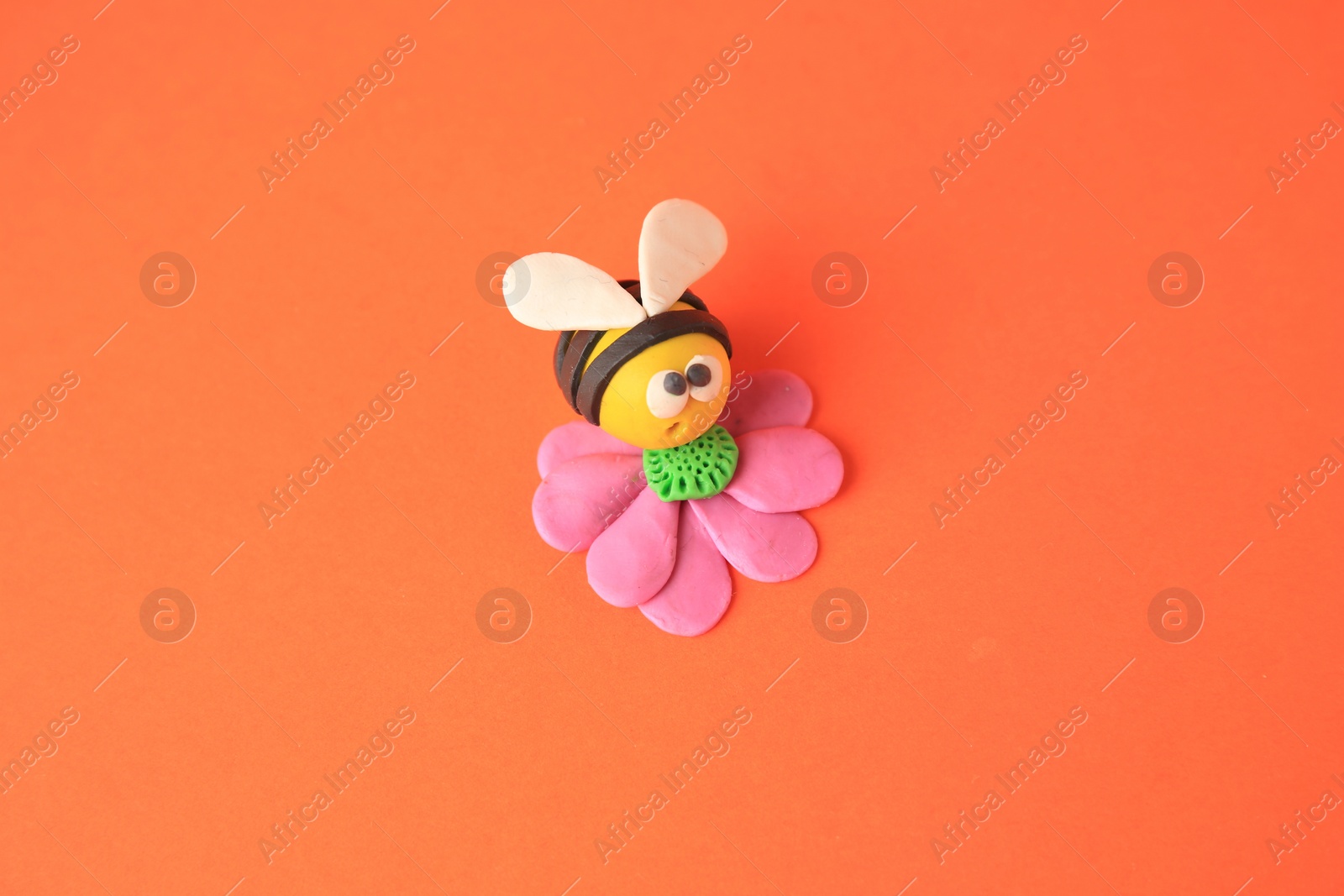 Photo of Bee with flower made from plasticine on orange background. Children's handmade ideas