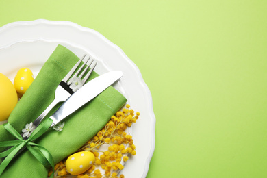 Festive Easter table setting with floral decor on green background, top view. Space for text