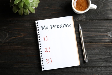 Image of Notebook with dreams list on dark wooden table, flat lay 