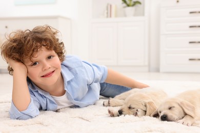 Photo of Little boy lying with cute puppies on white carpet at home