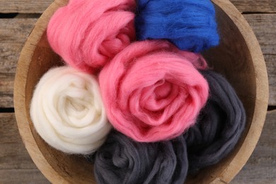 Photo of Colorful felting wool in bowl on wooden table, top view