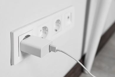 Photo of Charger adapter plugged in power socket indoors, closeup. Space for text