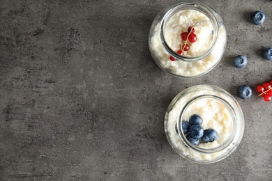 Photo of Creamy rice pudding with red currant and blueberries in jars on grey background, top view. Space for text