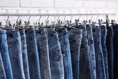 Rack with stylish jeans near brick wall, closeup