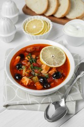 Photo of Meat solyanka soup with sausages, olives and vegetables served on white wooden table, above view