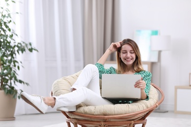 Attractive young woman with laptop in armchair at home