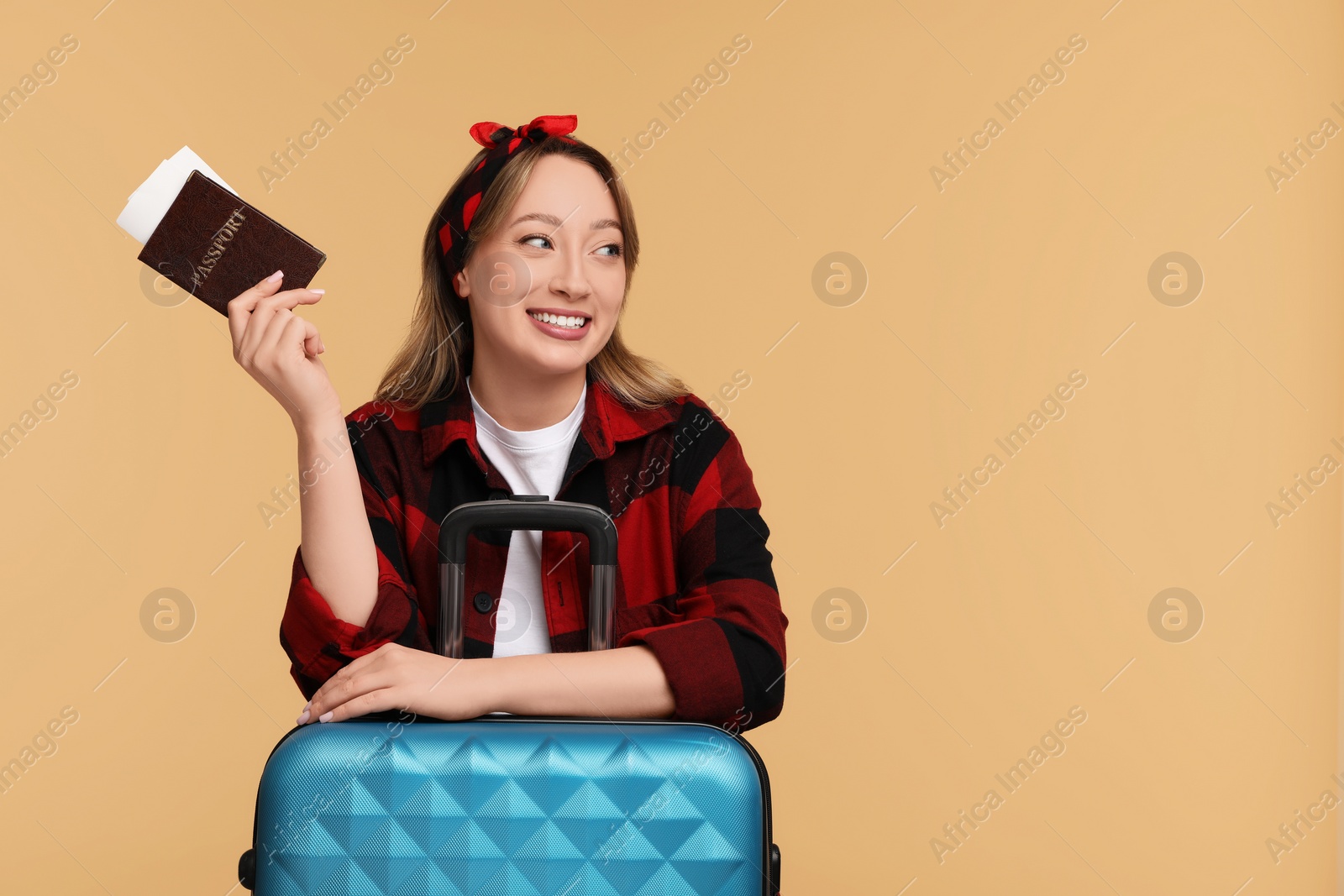 Photo of Happy young woman with passport, ticket and suitcase on beige background, space for text