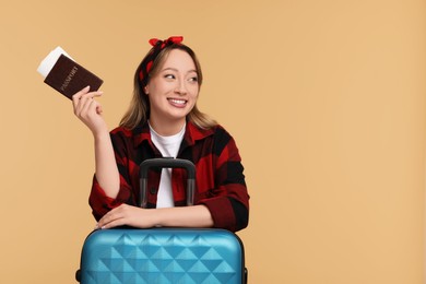 Photo of Happy young woman with passport, ticket and suitcase on beige background, space for text