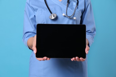 Closeup view of doctor with stethoscope holding blank tablet on light blue background, space for design. Cardiology concept