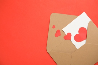 Photo of Envelope, card and paper hearts on red background, top view with space for text. Love letter