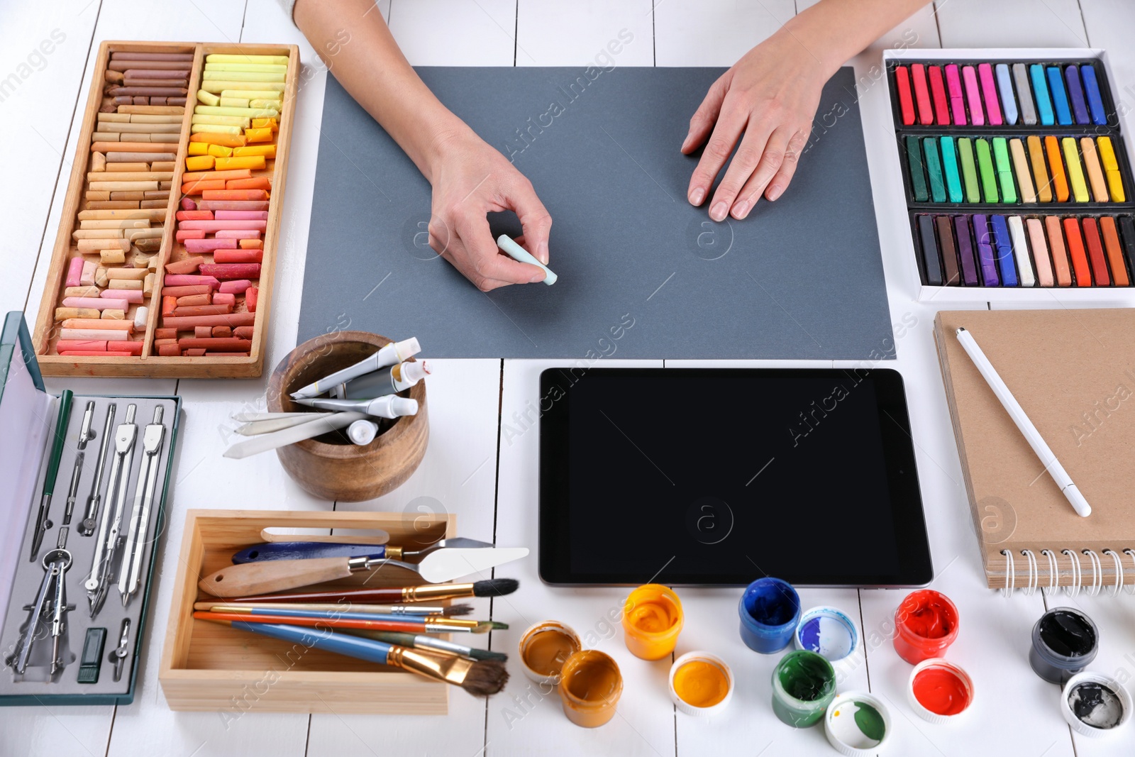 Photo of Artist drawing with chalk pastel on grey paper at white wooden table, above view