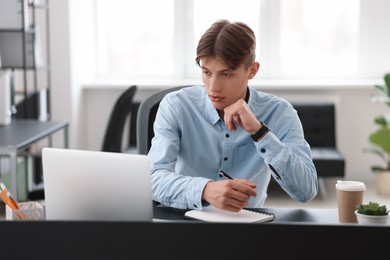 Photo of Man taking notes during webinar at table in office