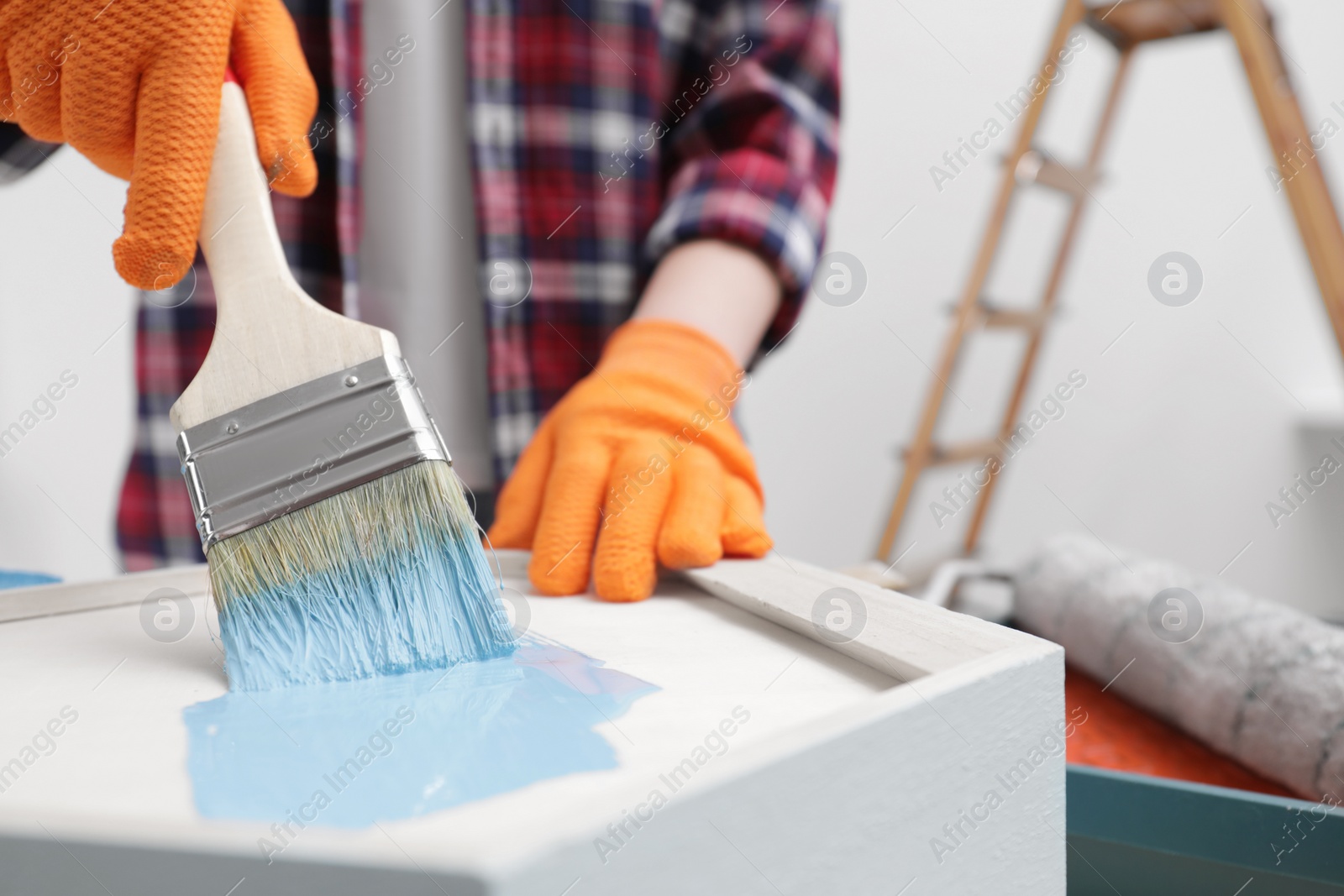 Photo of Woman painting shelf with brush indoors, closeup