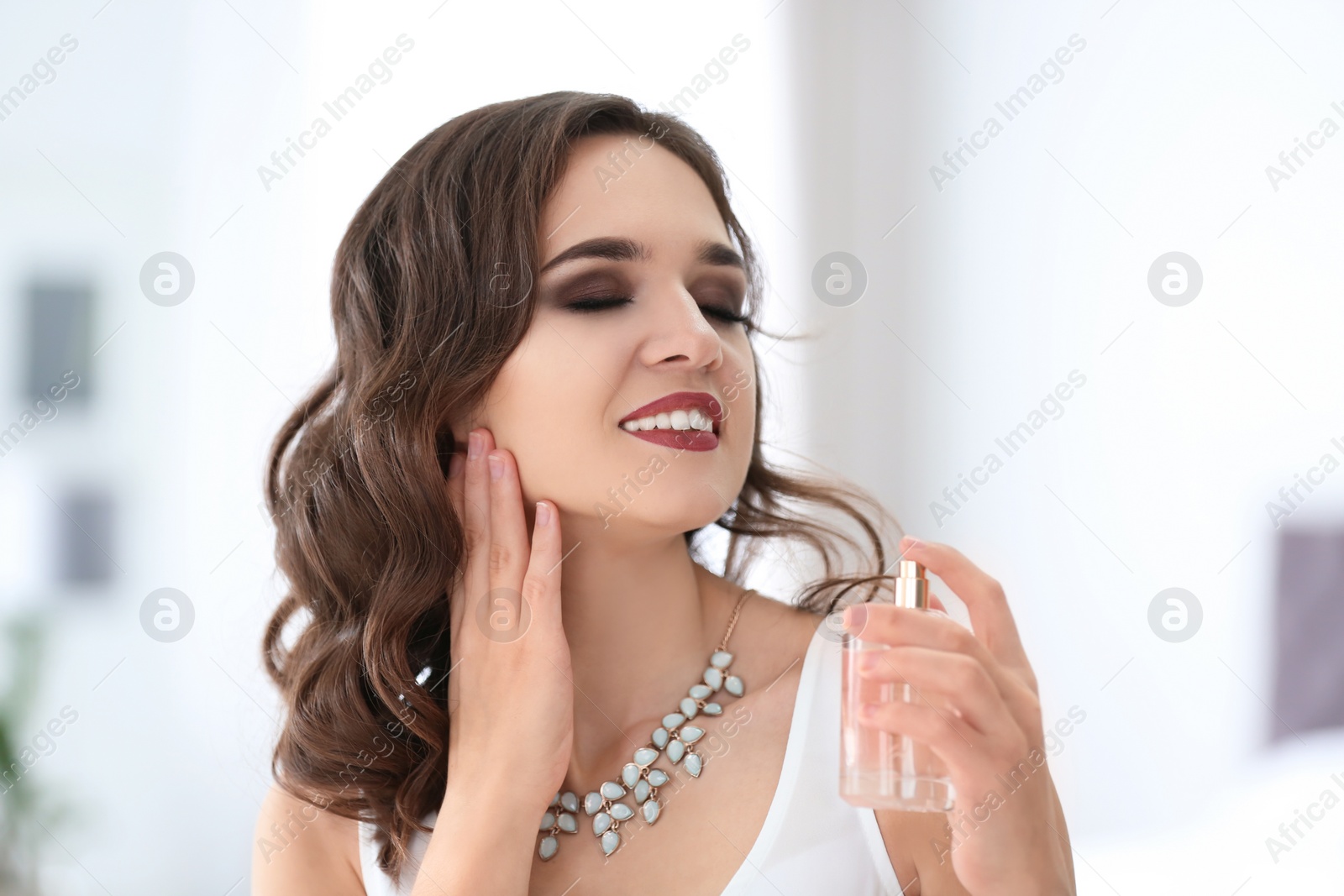 Photo of Beautiful young woman with bottle of perfume on blurred background