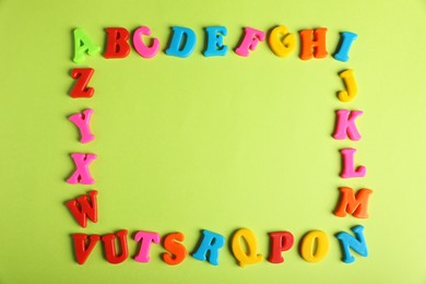 Photo of Frame made of many colorful magnetic letters on light green background, flat lay with space for text