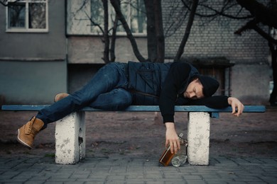 Addicted drunk man with alcoholic drink lying on bench outdoors