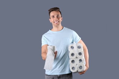 Young man holding toilet paper rolls on color background