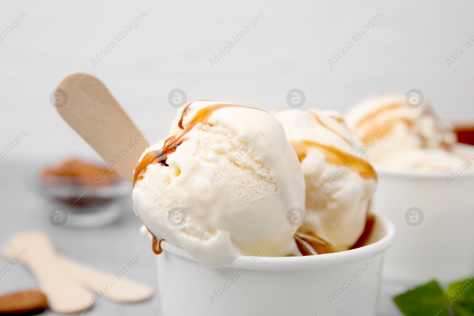 Photo of Scoops of ice cream with caramel sauce in paper cup, closeup