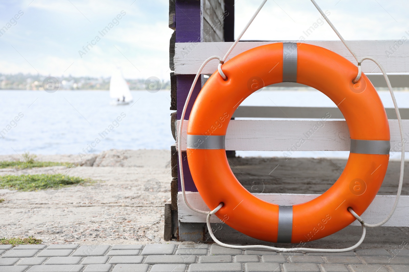 Photo of Orange life buoy hanging on white wooden fence at beach, space for text