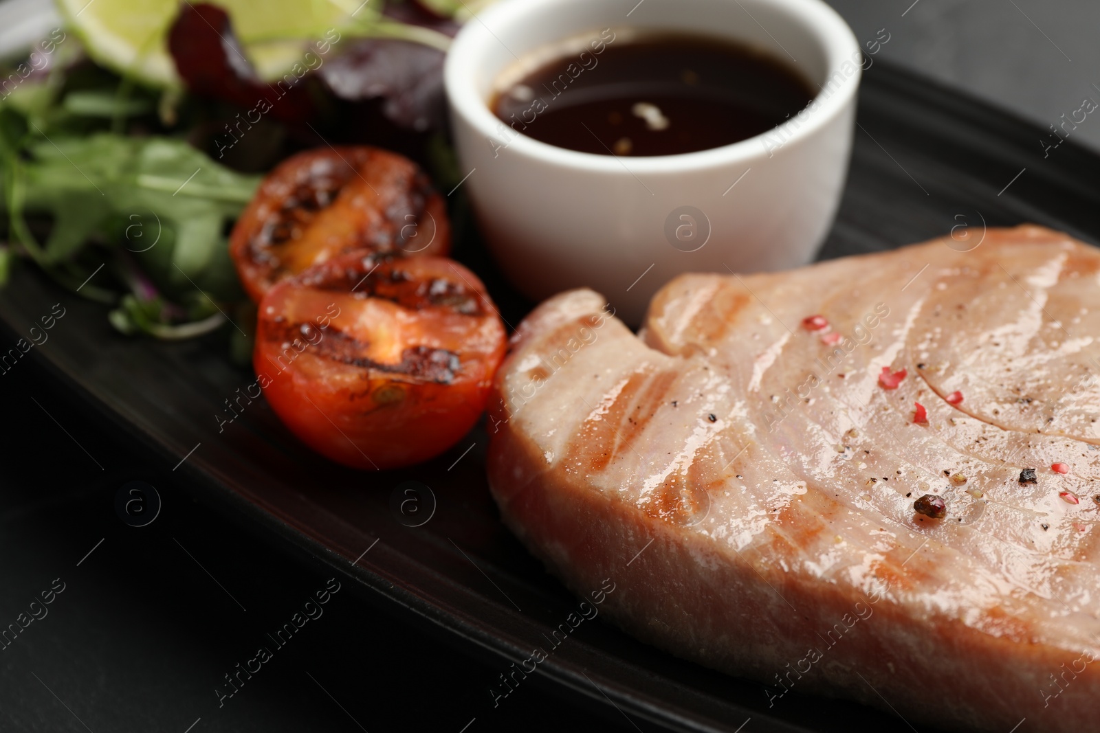 Photo of Delicious tuna steak, tomato and sauce on table, closeup