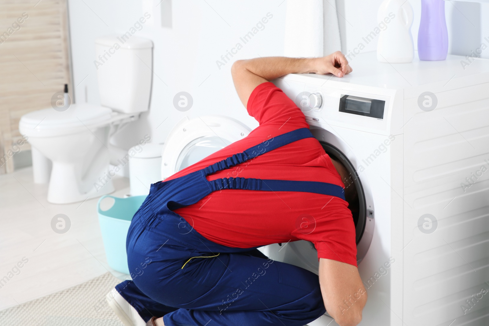 Photo of Young plumber examining washing machine in bathroom