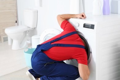 Photo of Young plumber examining washing machine in bathroom