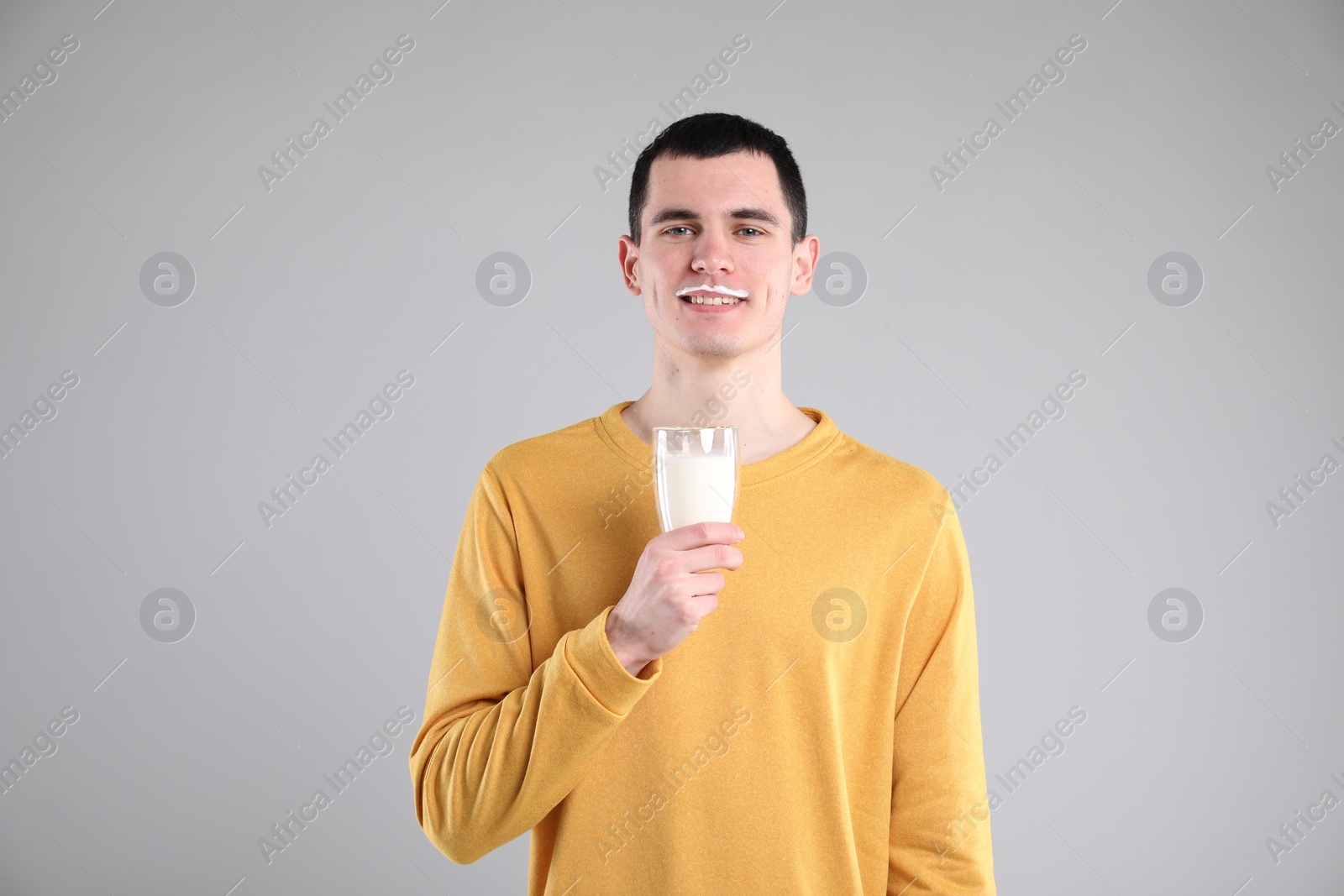 Photo of Happy man with milk mustache holding glass of tasty dairy drink on gray background