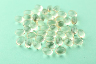 Photo of Many vitamin capsules on turquoise background, closeup
