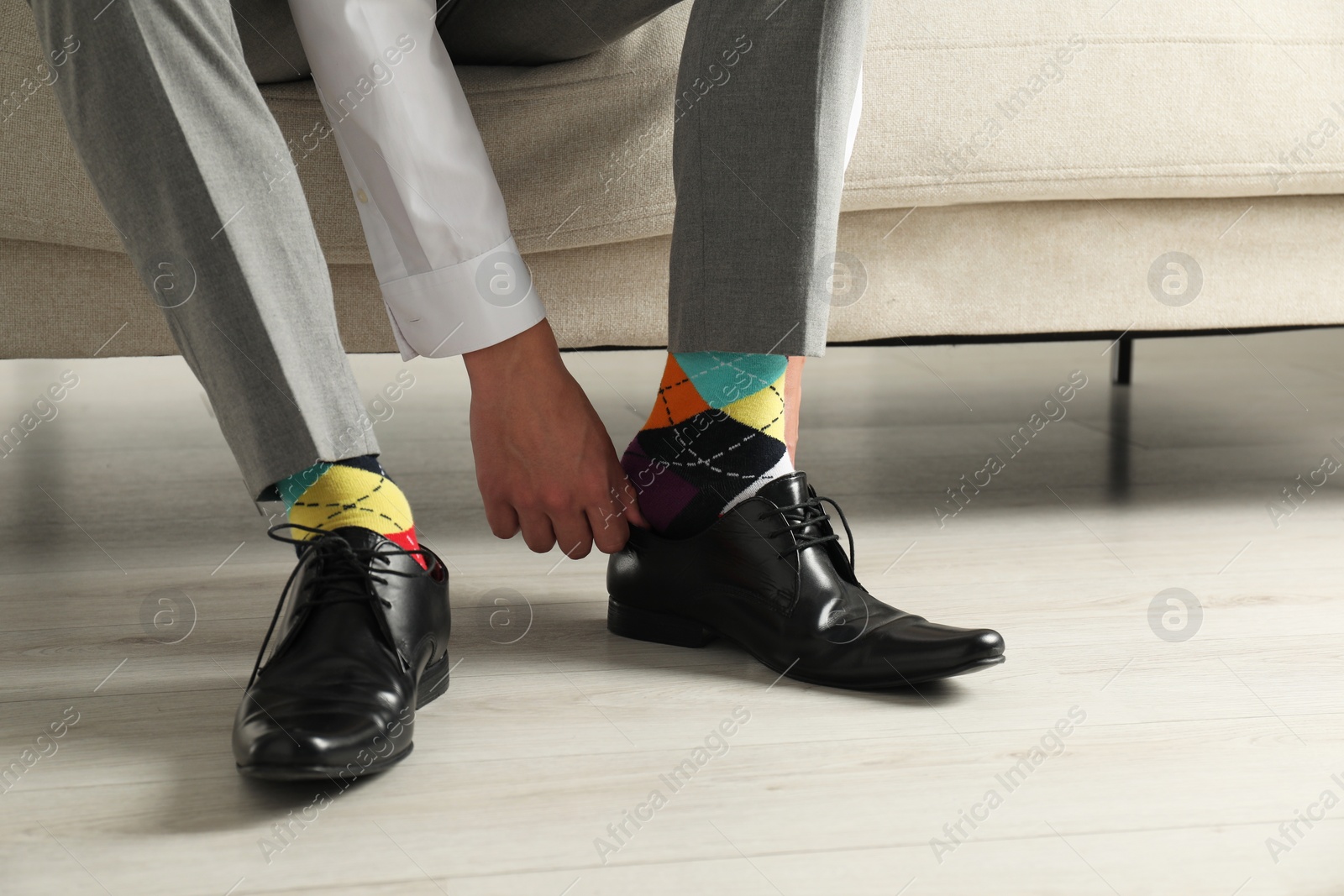 Photo of Man with colorful socks putting on stylish shoes indoors, closeup