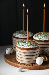 Photo of Traditional Easter cakes with sprinkles, candles and decorated eggs on white wooden table