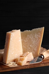 Photo of Parmesan cheese with board and knife on black wooden table