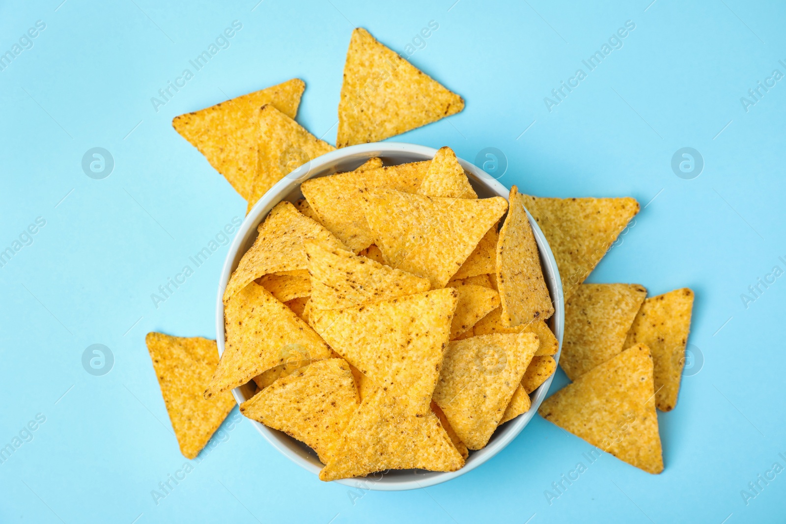Photo of Bowl with tasty Mexican nachos chips on light blue background, flat lay